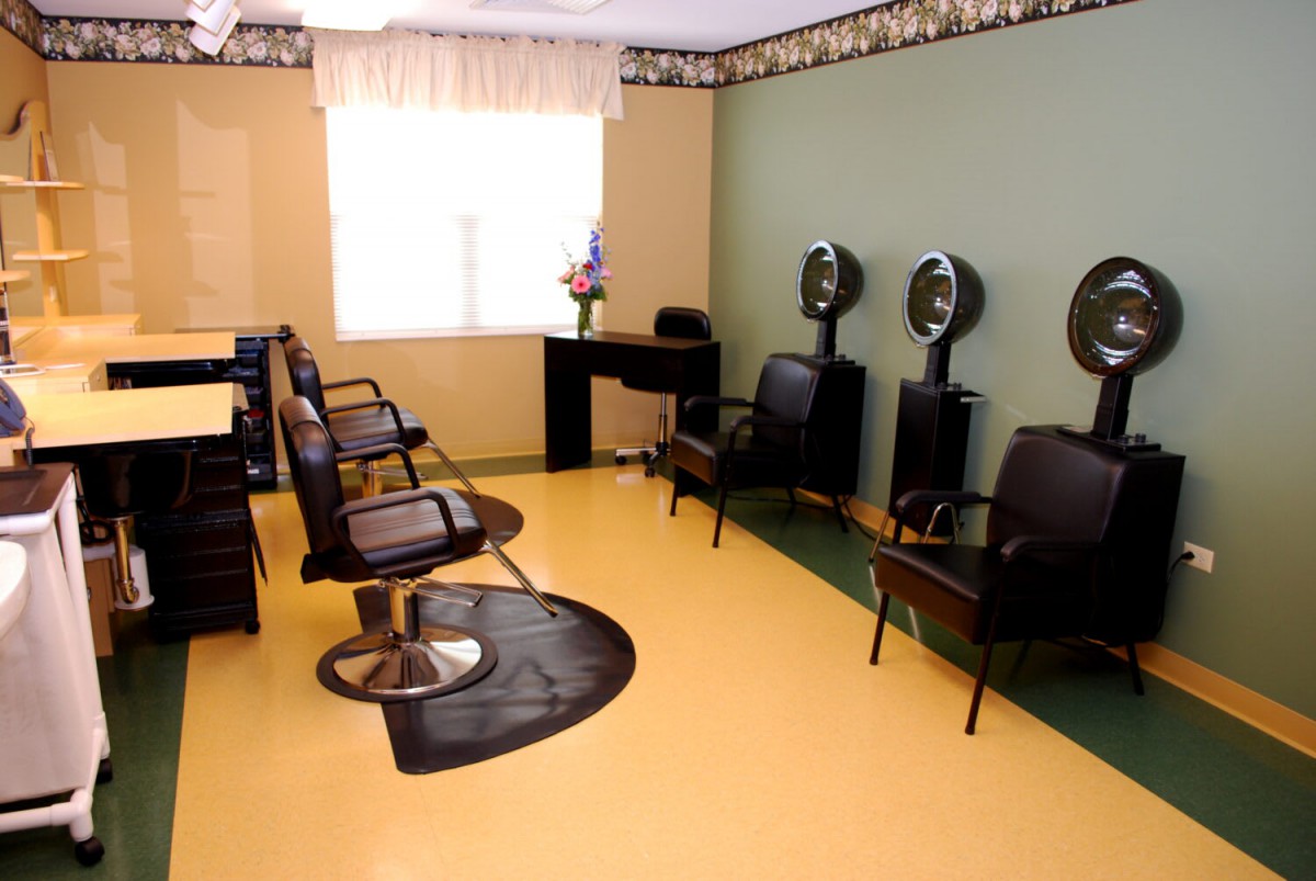 An empty hair salon with chairs, styling stations, and hair dryers lining the walls.