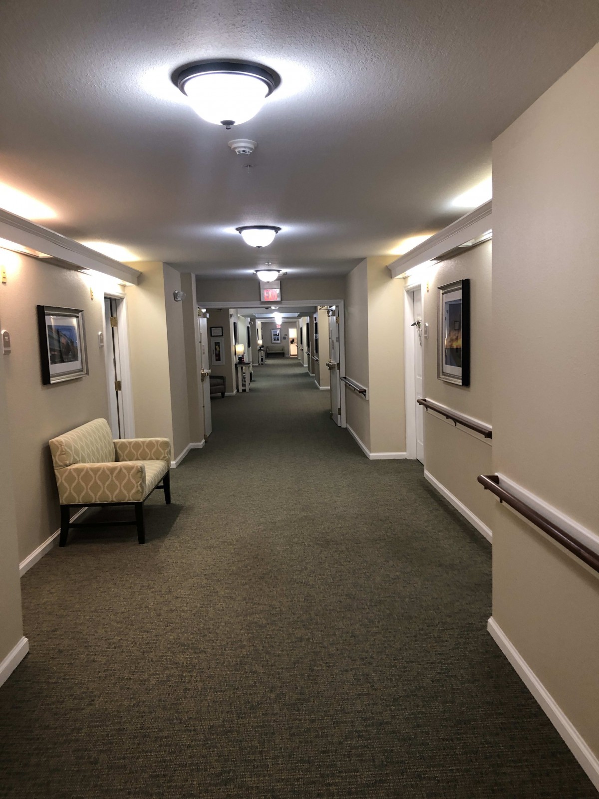 A well-lit, carpeted hallway with several doors and a chair along the wall.