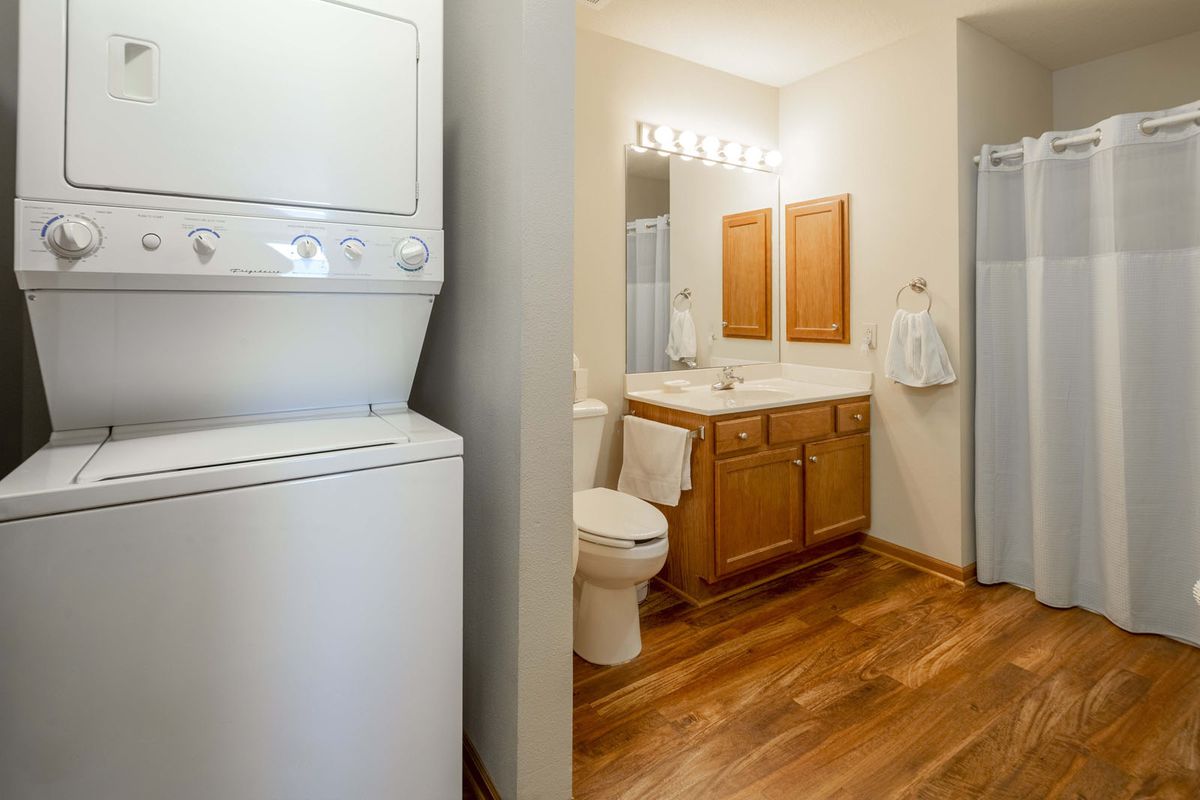 A bathroom with a stacked washer and dryer unit, wooden flooring, and a sink with a mirror.