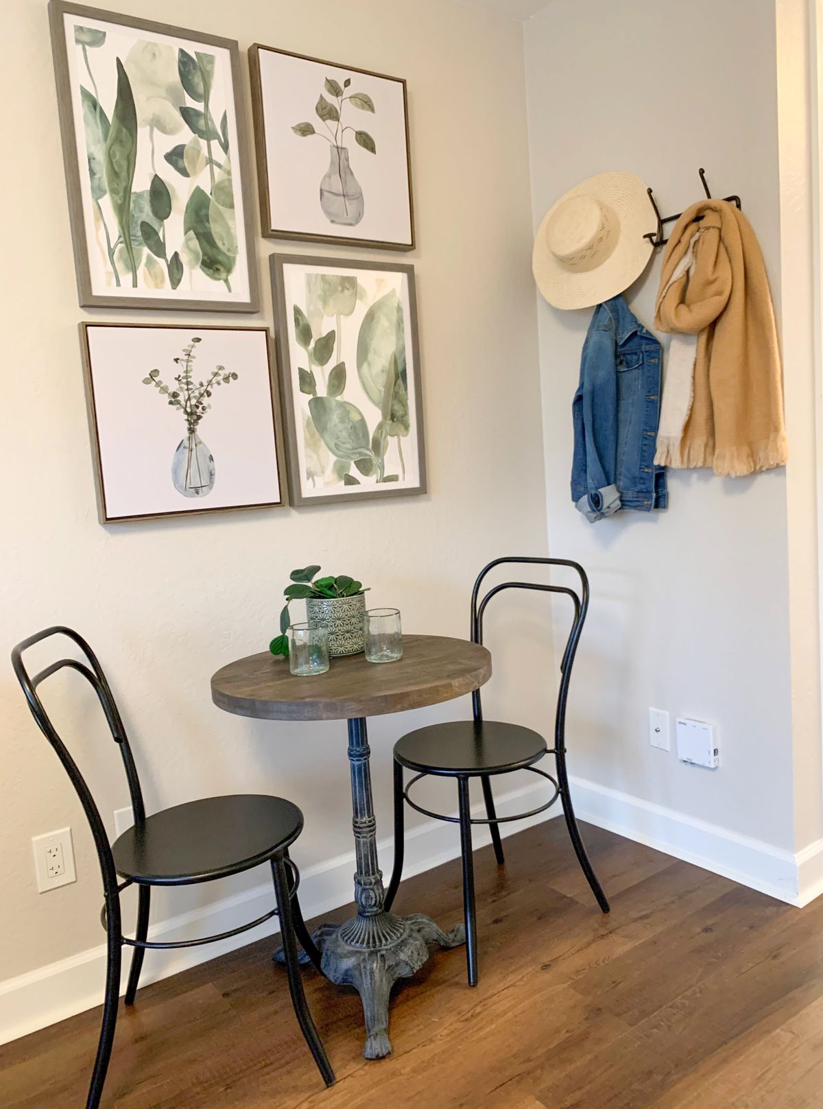 A cozy corner with a small table and chairs, adorned with botanical wall art and hanging hats and jackets.