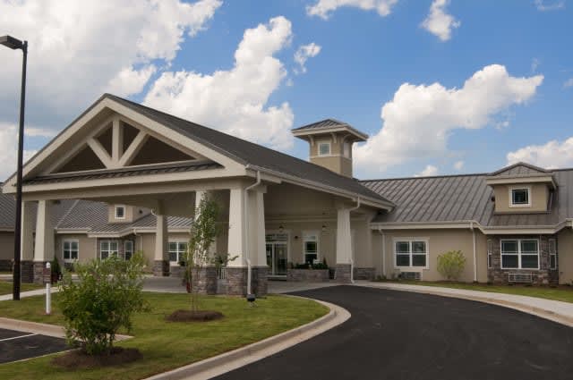 A modern building with a covered entrance and landscaped surroundings under a partly cloudy sky.