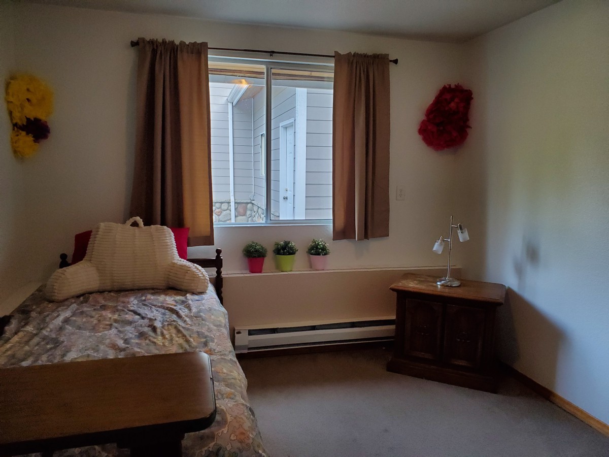 A cozy bedroom with a bed, pillows, and a nightstand next to a window adorned with curtains.
