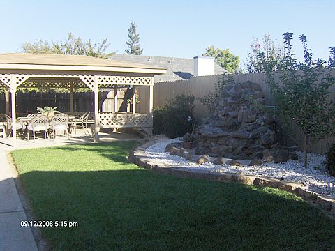 A backyard with a pergola, green lawn, and garden landscaping.
