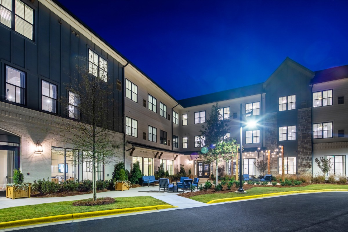 A modern building illuminated at night, featuring a well-kept exterior and landscaped surroundings.