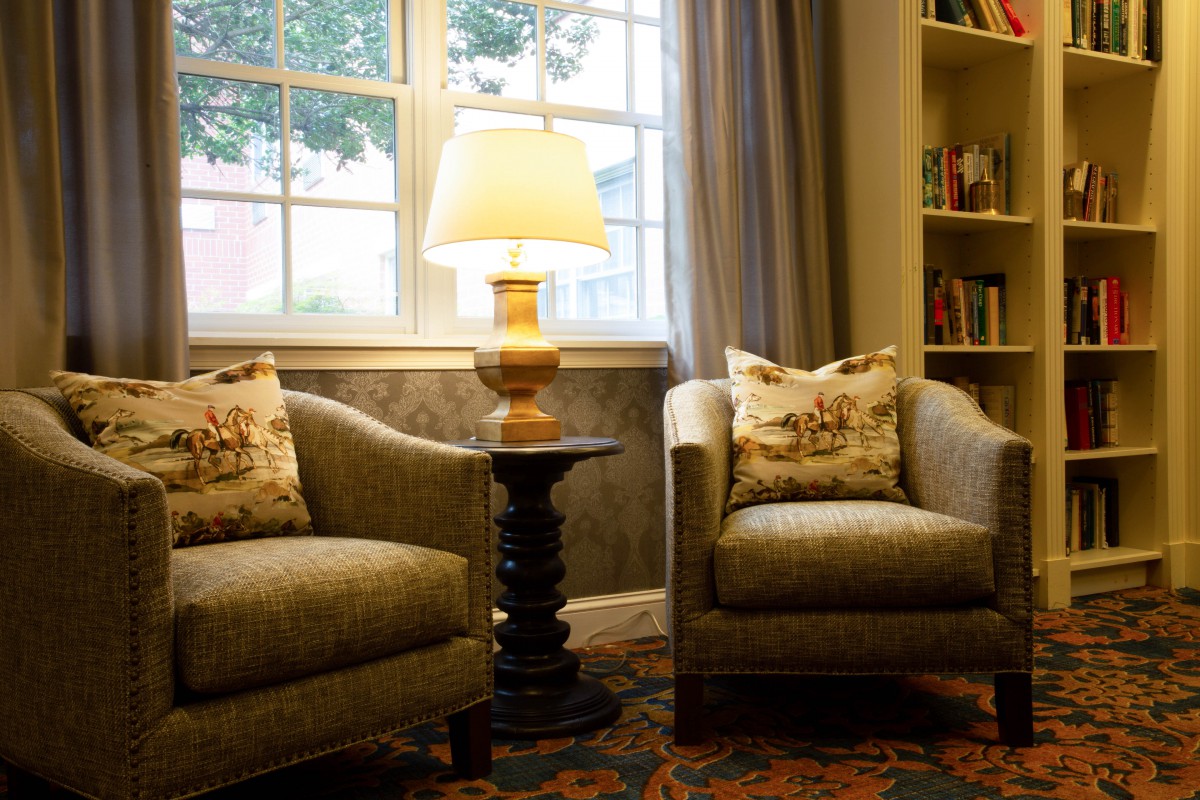 A cozy living room setting with two armchairs, a lamp on a side table, and a window in the background.