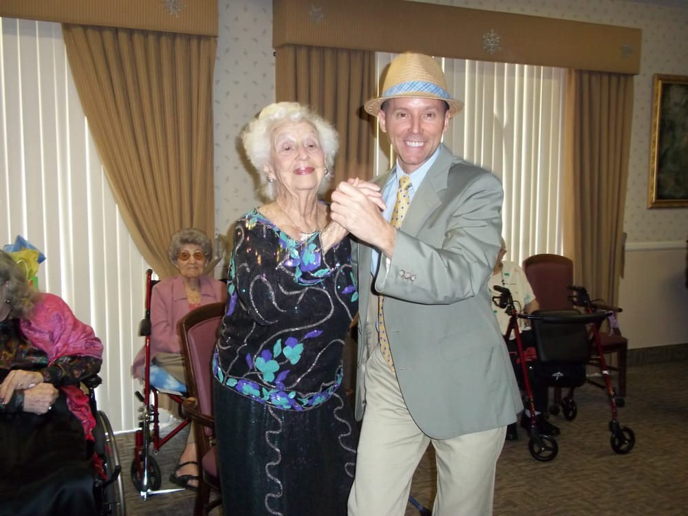 An older woman and a man are happily dancing together indoors at an event.