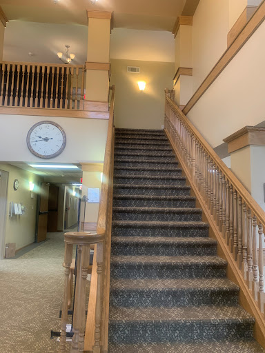 A view of a staircase with wooden railing leading to an upper floor, featuring a clock on the wall.
