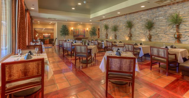 Elegant restaurant interior with neatly arranged tables and chairs, featuring a decorative brick wall and potted plants.