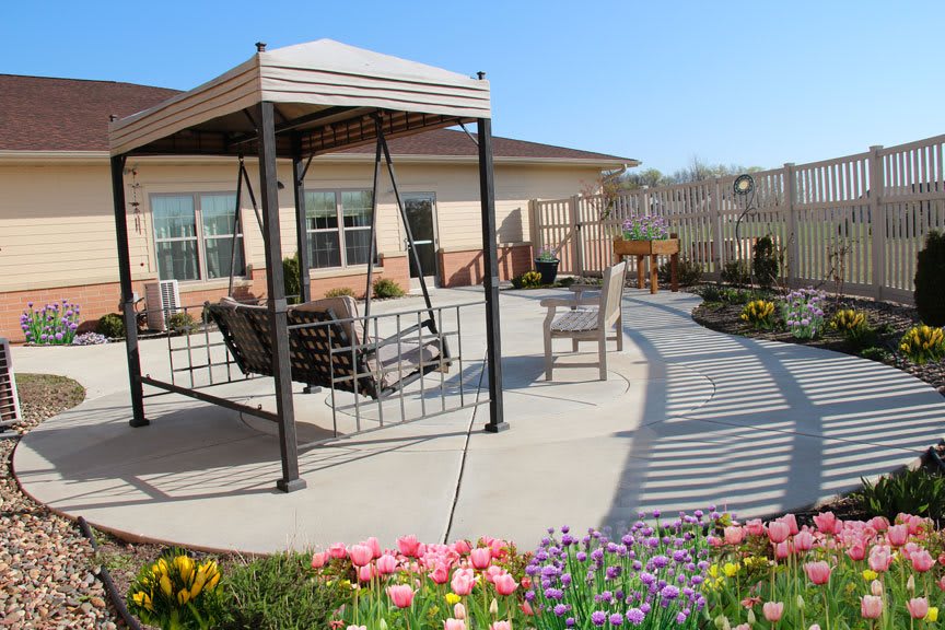 A cozy patio area with a swing under a pergola, surrounded by colorful flowers.