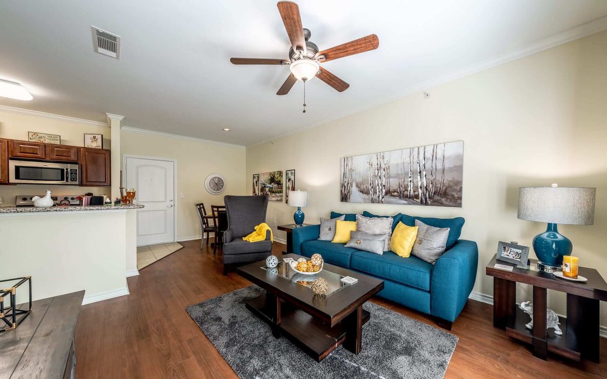 A modern living room with a teal sofa and yellow pillows, featuring a coffee table and ceiling fan.