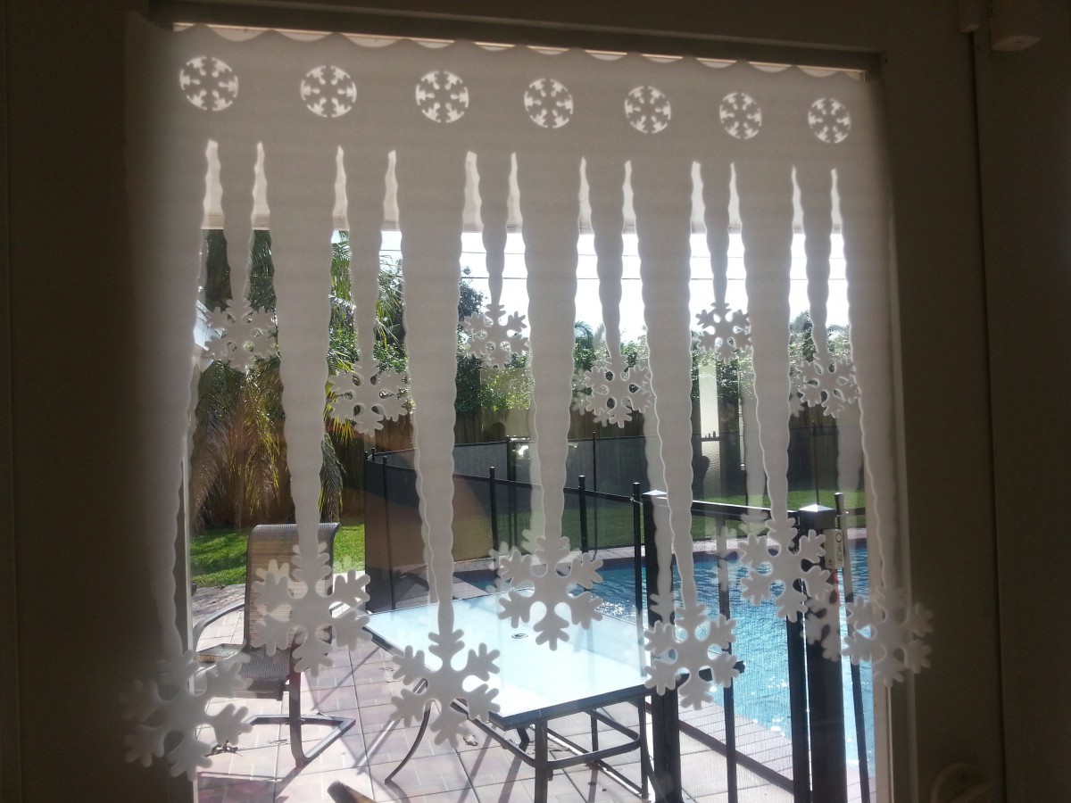 A lace curtain with snowflake patterns hangs in front of a window overlooking a backyard pool and outdoor furniture.