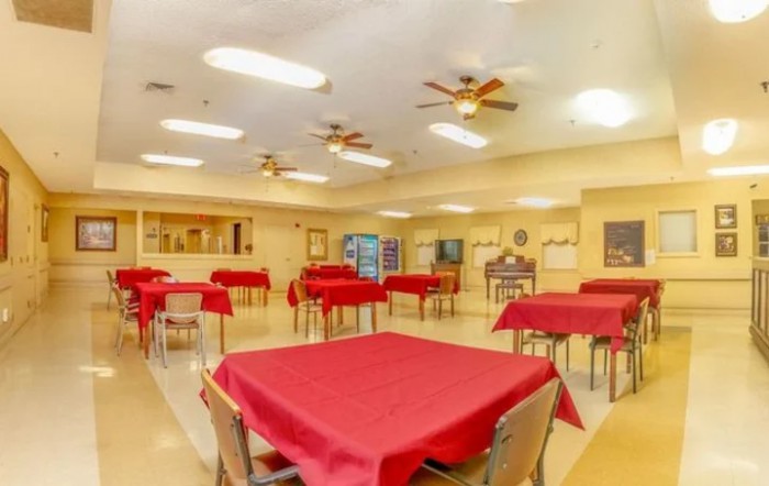A spacious dining hall with red tablecloths on each table and ceiling fans overhead.