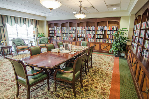A cozy library space featuring a large wooden table surrounded by chairs, with shelves filled with books in the background.