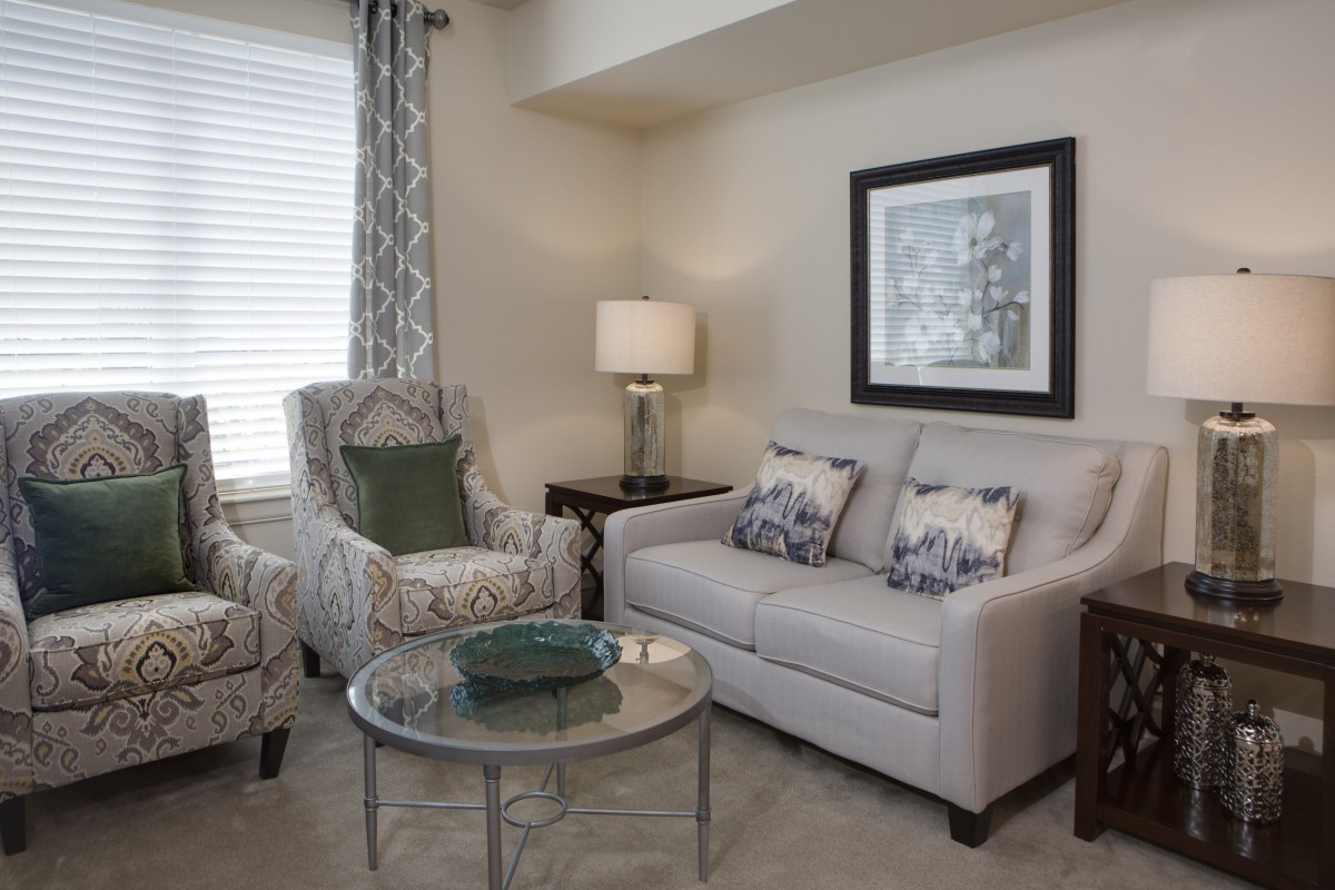 A cozy living room with a sofa, armchair, and coffee table, complemented by a lamp and artwork on the wall.