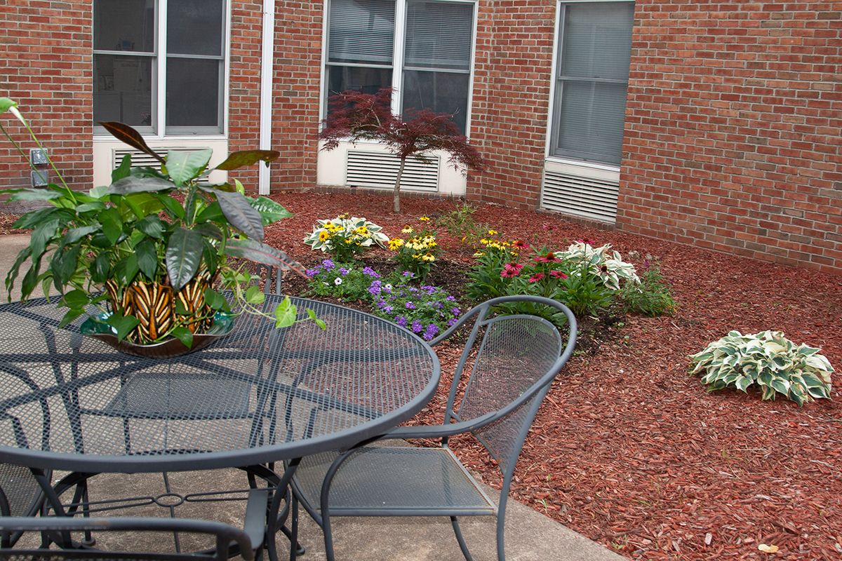 A cozy patio garden with outdoor furniture and vibrant flowers against a brick building backdrop.