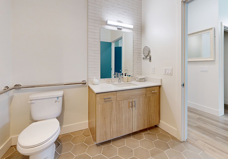 A modern bathroom with a wooden vanity, sink, mirror, and toilet.
