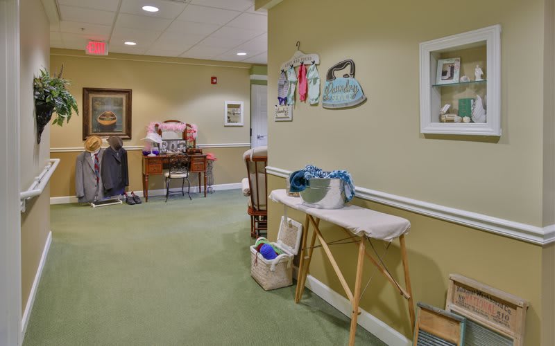 A cozy hallway with an ironing board, decorative items on the wall, and green carpeting.