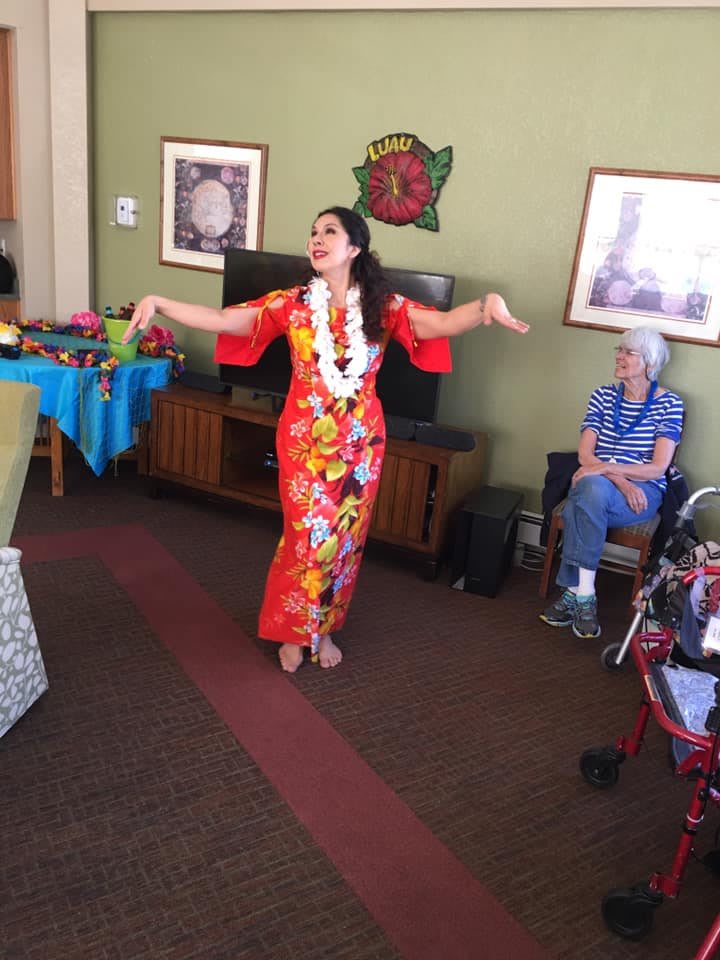 A woman performs a hula dance in front of an audience indoors.