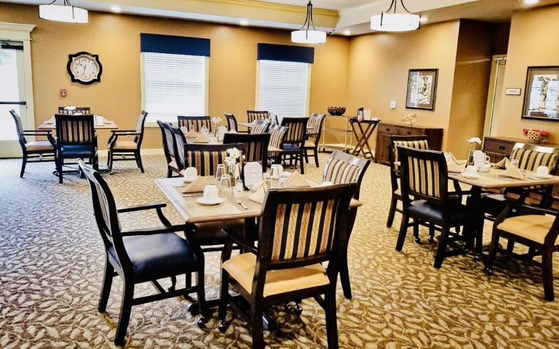 A cozy dining room with neatly arranged tables and chairs, featuring warm neutral tones.