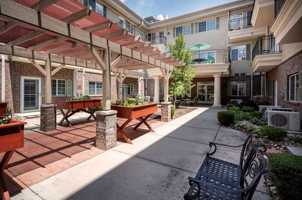 A sunny courtyard with benches and a pergola in an outdoor area surrounded by a multi-story building.