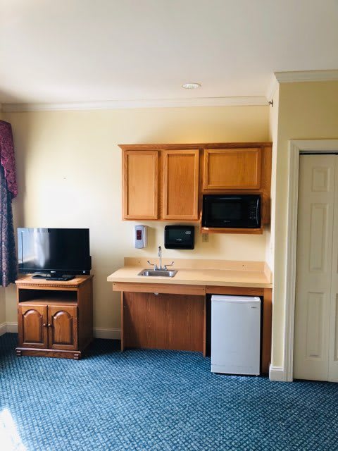 A small kitchenette area in a hotel room featuring a TV, microwave, sink, and refrigerator.