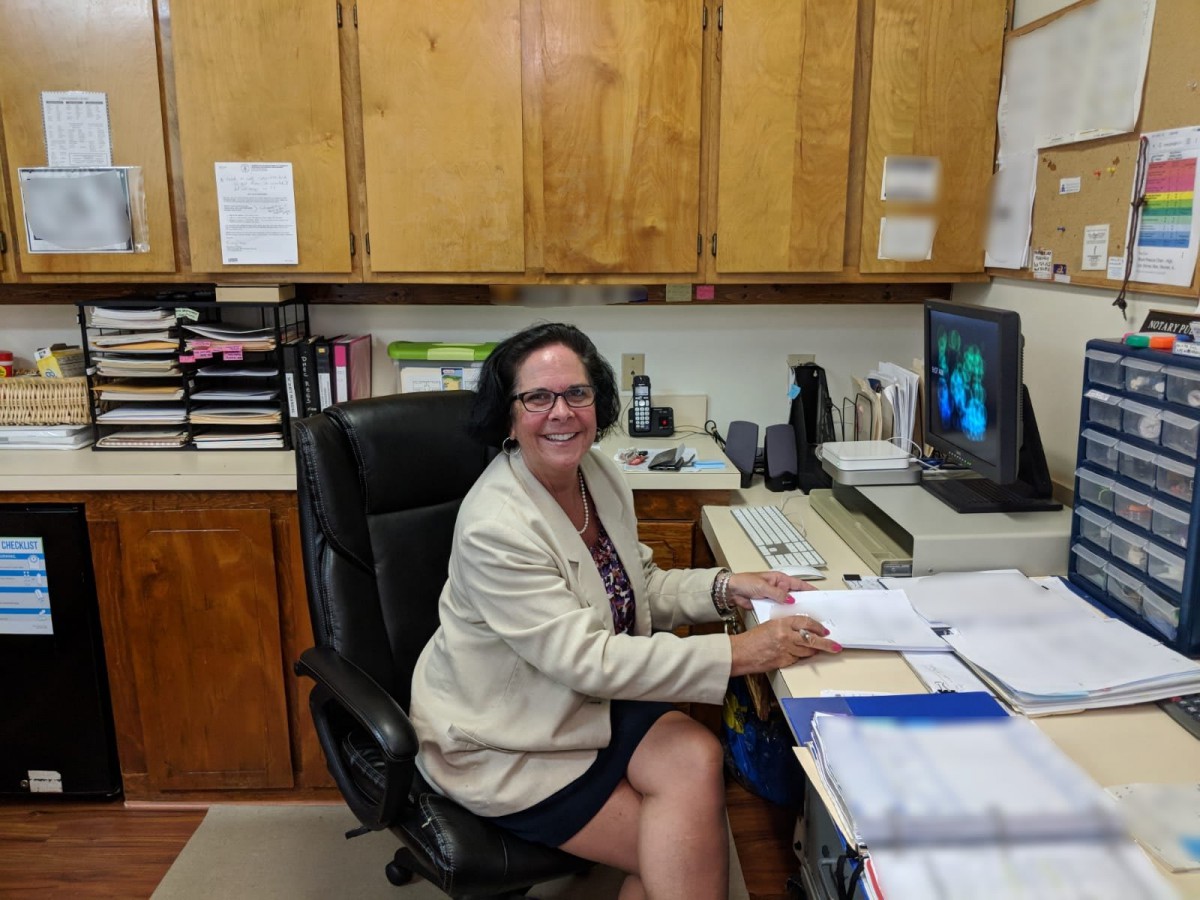 A woman sitting at a desk in an office environment, surrounded by files and using a computer.