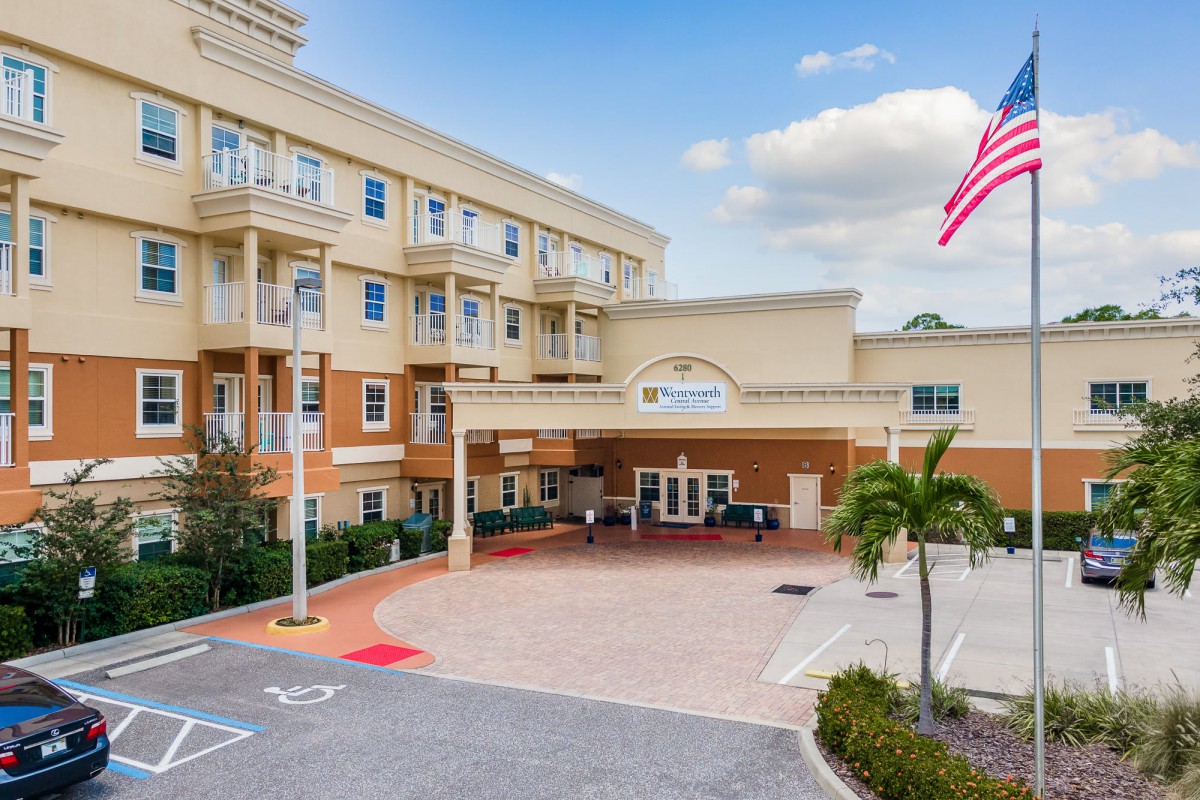 A multi-story building with a grand entrance, featuring an American flag and surrounded by palm trees.