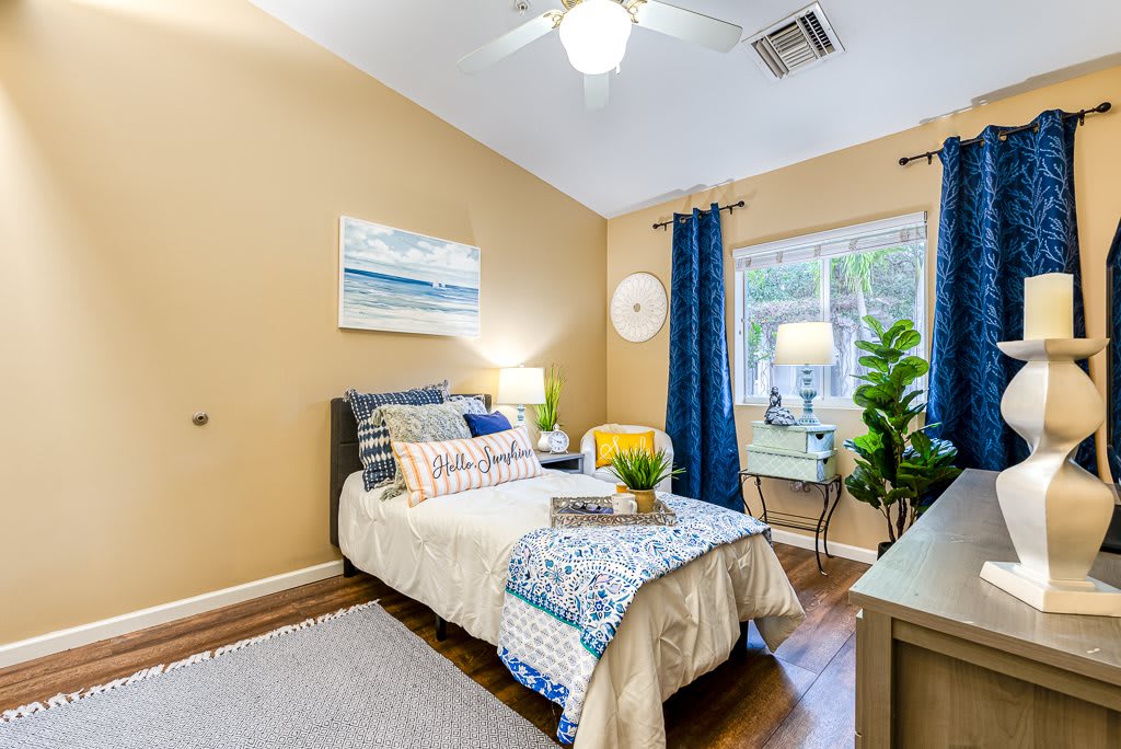 A cozy and well-decorated bedroom featuring a comfortable bed, indoor plants, and a large window with blue curtains.