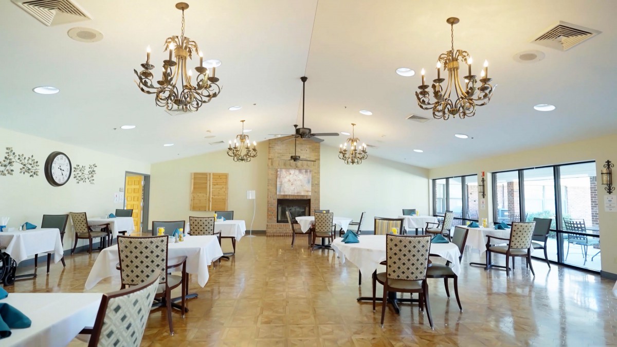 A spacious dining area with elegant chandeliers, neatly arranged tables, and patterned chairs.