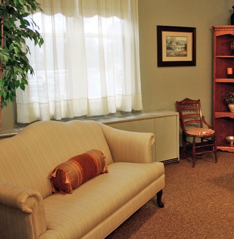 A cozy living room with a comfortable sofa, decorative pillows, and a bookshelf beside a window with sheer curtains.