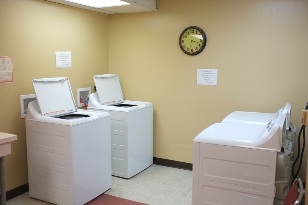 A well-lit laundry room featuring several washing machines with open lids.