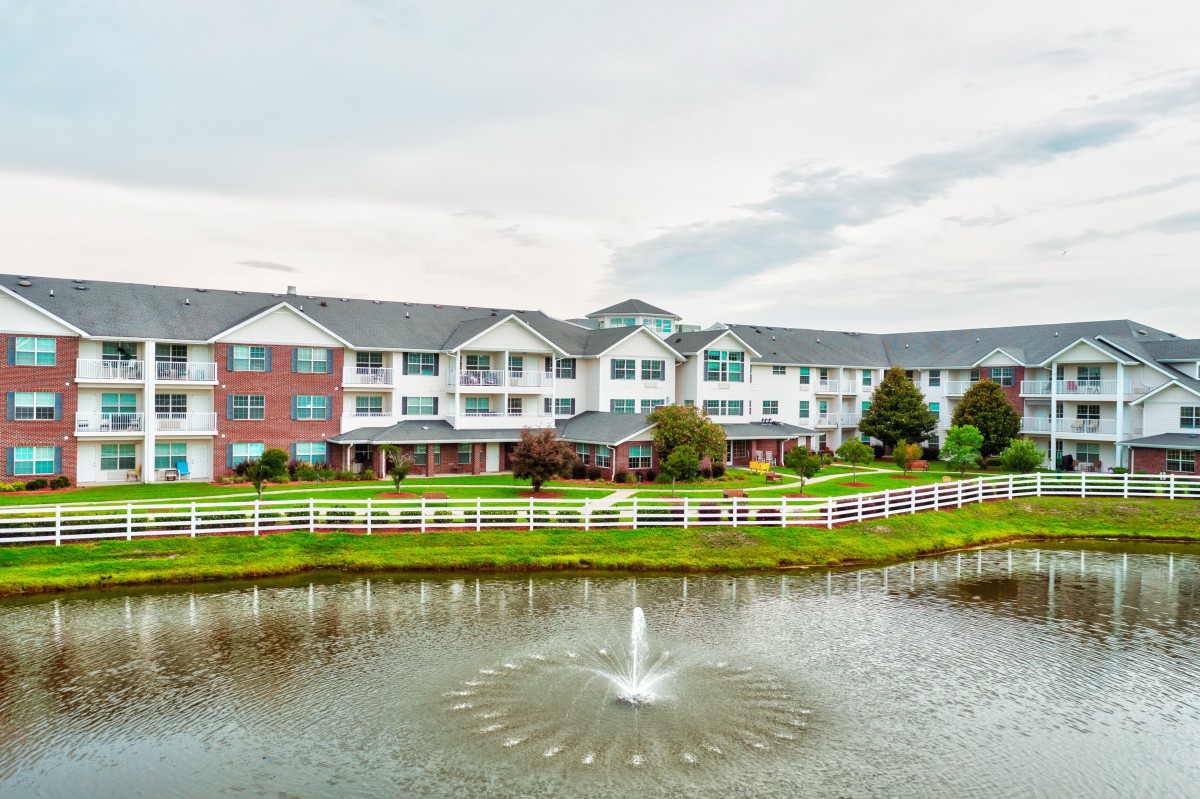 A scenic view of a residential building with a fountain in a pond in the foreground.