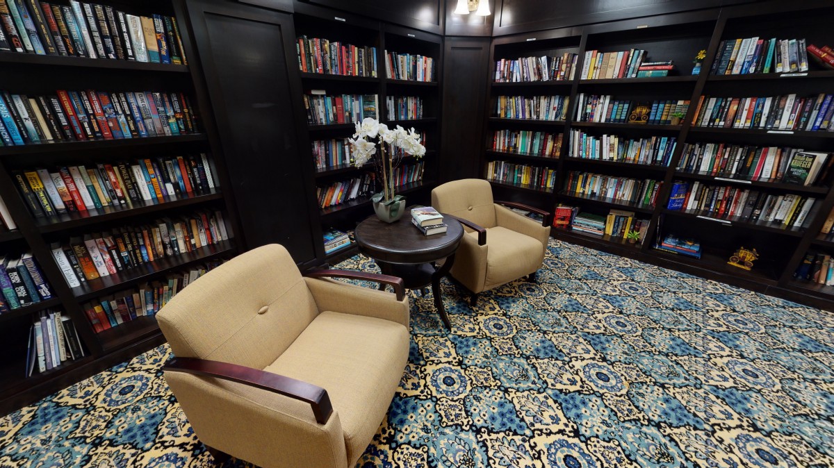 A cozy library corner with two comfortable chairs and a table surrounded by bookshelves.