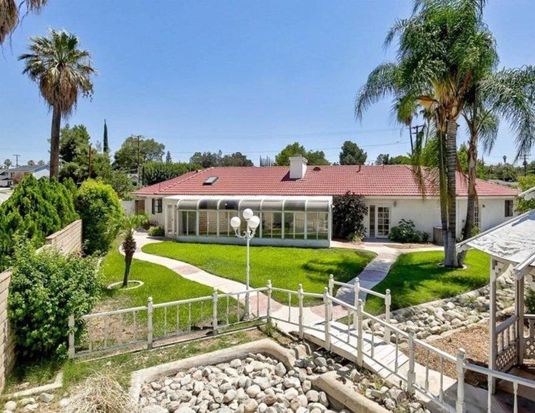 A view of a house with a spacious backyard featuring a green lawn, pathway, and palm trees.
