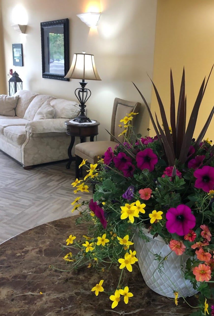 A cozy lobby area featuring a plush sofa, side table with a lamp, and a vibrant floral arrangement.