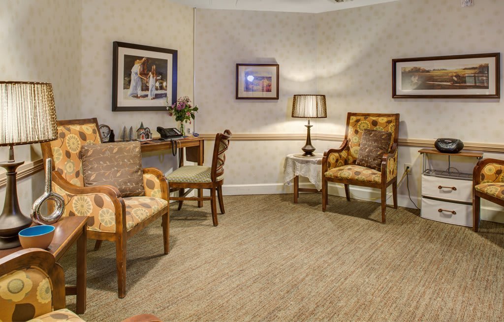 A cozy interior featuring elegant chairs, a small table with decor, a lamp, and framed artwork on the walls.