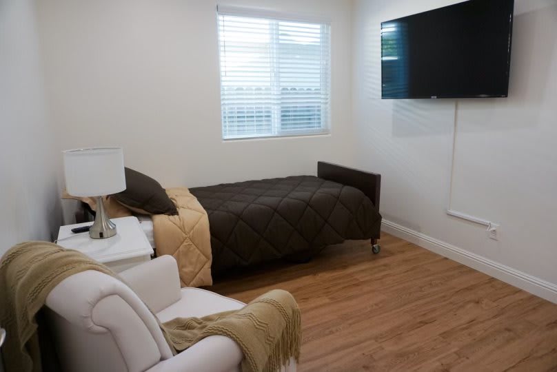 A cozy bedroom with a single bed, wall-mounted TV, and wooden flooring.