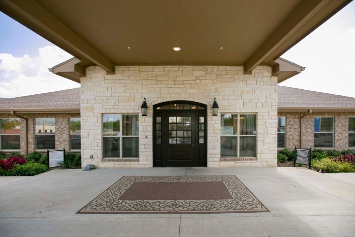 The entrance of a modern stone building with large windows and a central door.