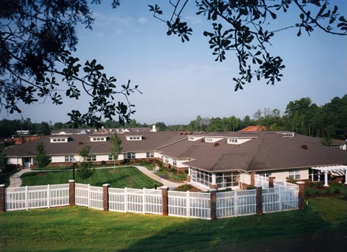 A scenic view of a large house with a white fence, surrounded by greenery and trees.