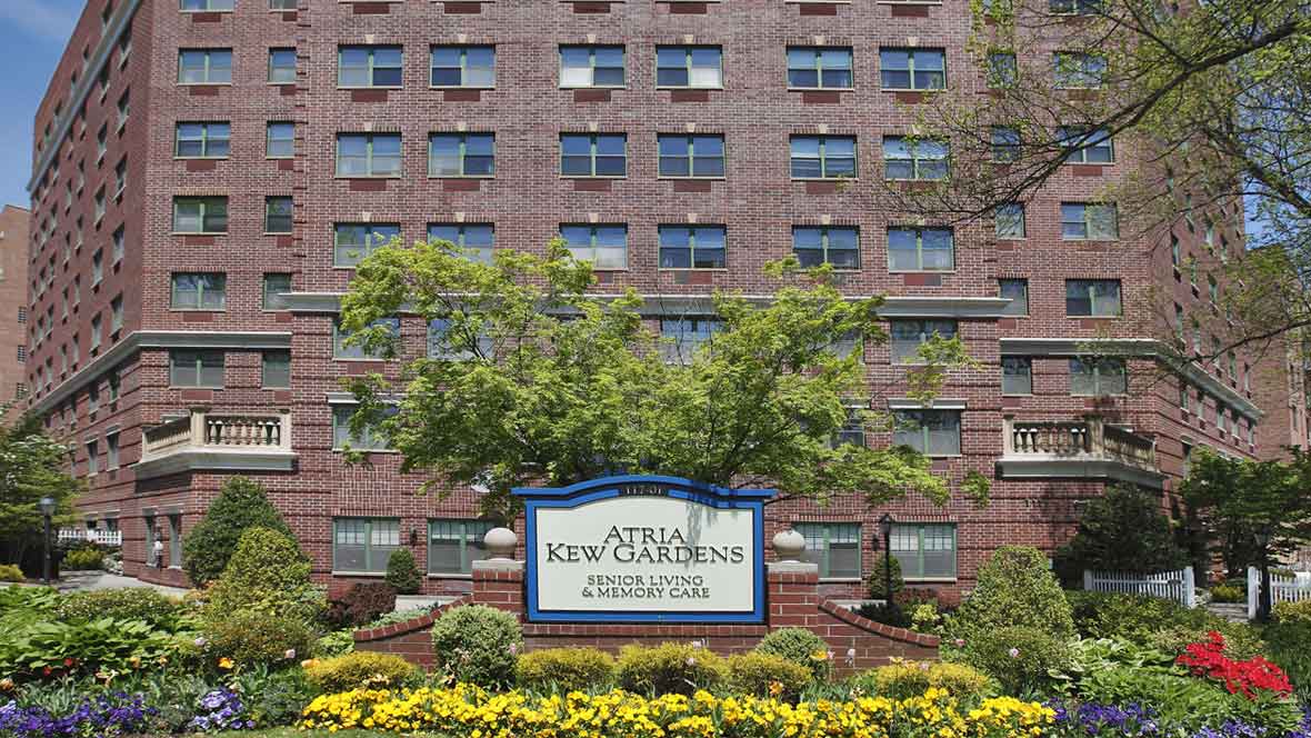 A brick building with a prominent sign and landscaping including trees and flowers.
