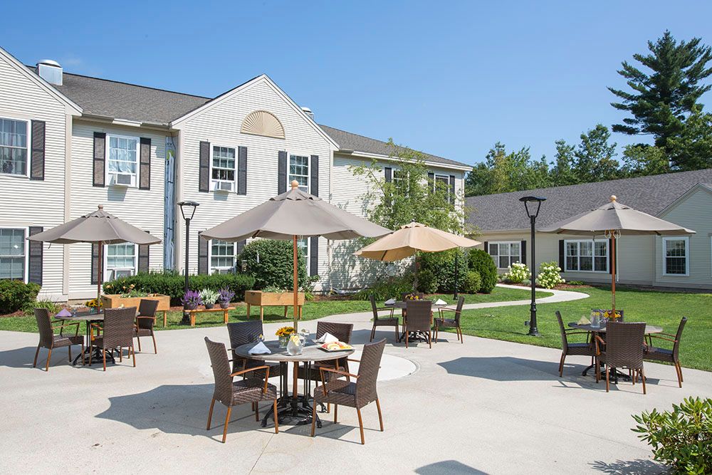 A sunny outdoor patio area with tables, chairs, and umbrellas in front of a building.