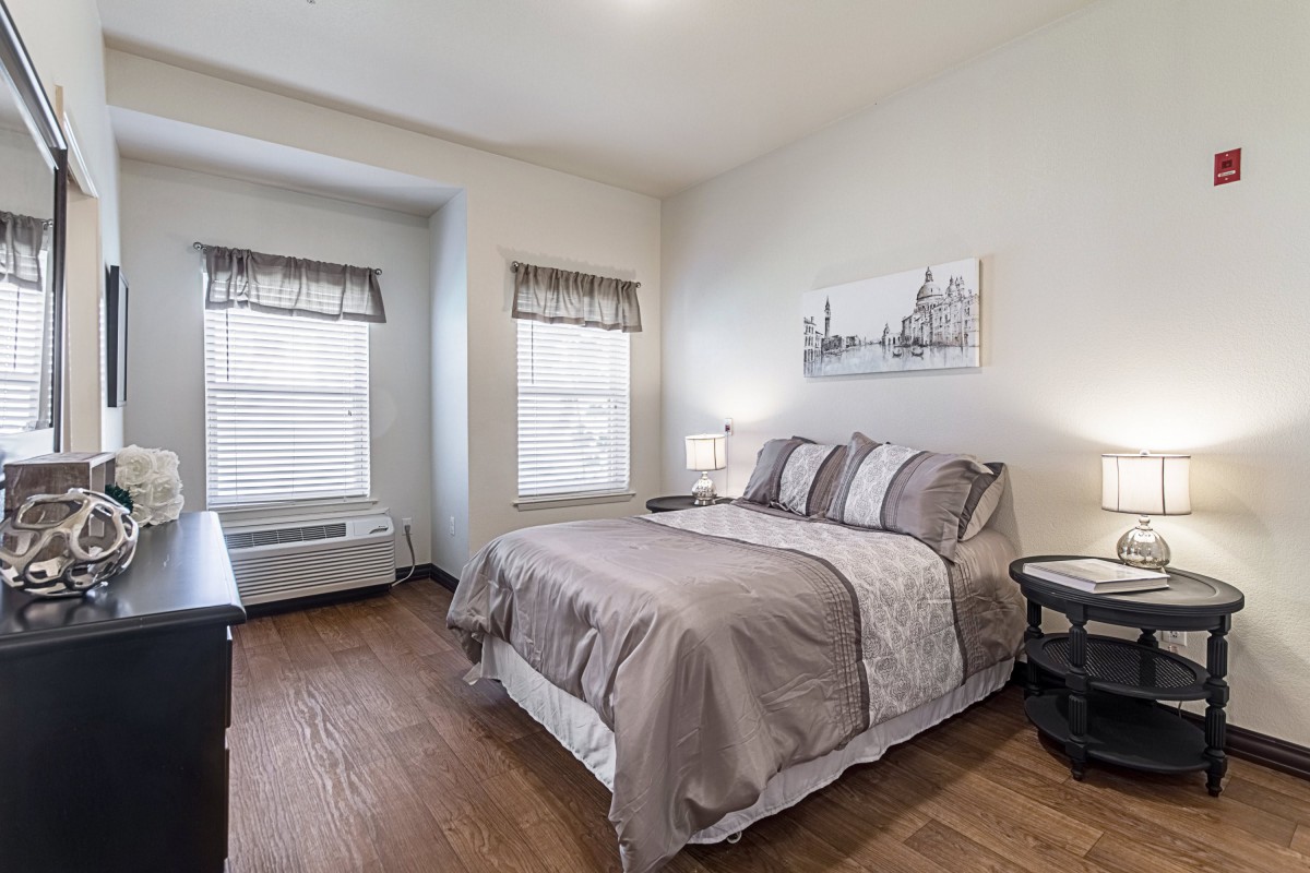 A modern, minimalist bedroom with a neatly made bed and wooden flooring.