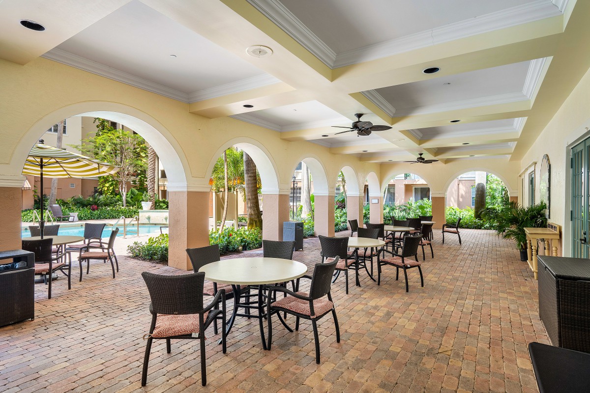 A spacious outdoor patio with tables and chairs under a covered area featuring arches and ceiling fans.