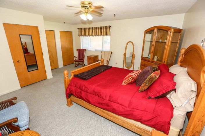 A cozy bedroom with a wooden bed frame featuring red bedding, surrounded by wooden furniture including a dresser and mirror.
