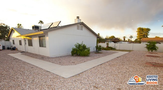 A suburban house with solar panels on the roof and a gravel yard.