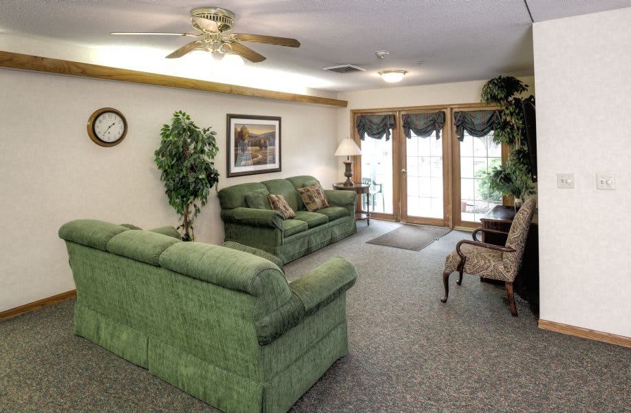 A cozy living room with green sofas, carpet flooring, and a ceiling fan.