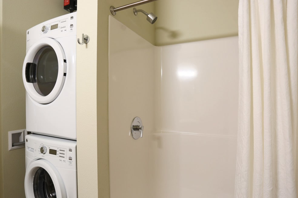 A compact laundry area with a stacked washer and dryer next to a shower.
