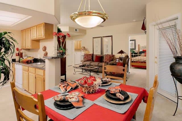 A cozy apartment interior featuring a dining table with vibrant red accents, an adjacent living room, and an open kitchen layout.