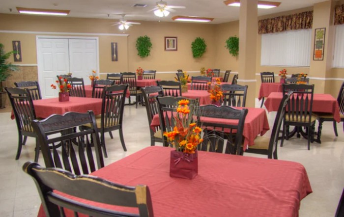 A neatly arranged dining area with tables covered in red tablecloths and floral centerpieces.