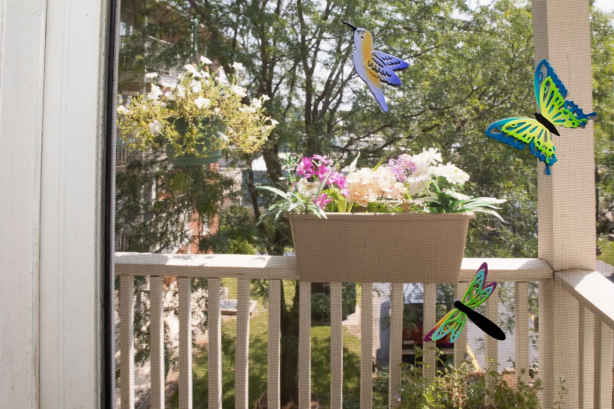 A colorful flower box adorns a balcony railing, surrounded by decorative ornaments and a lush tree in the background.